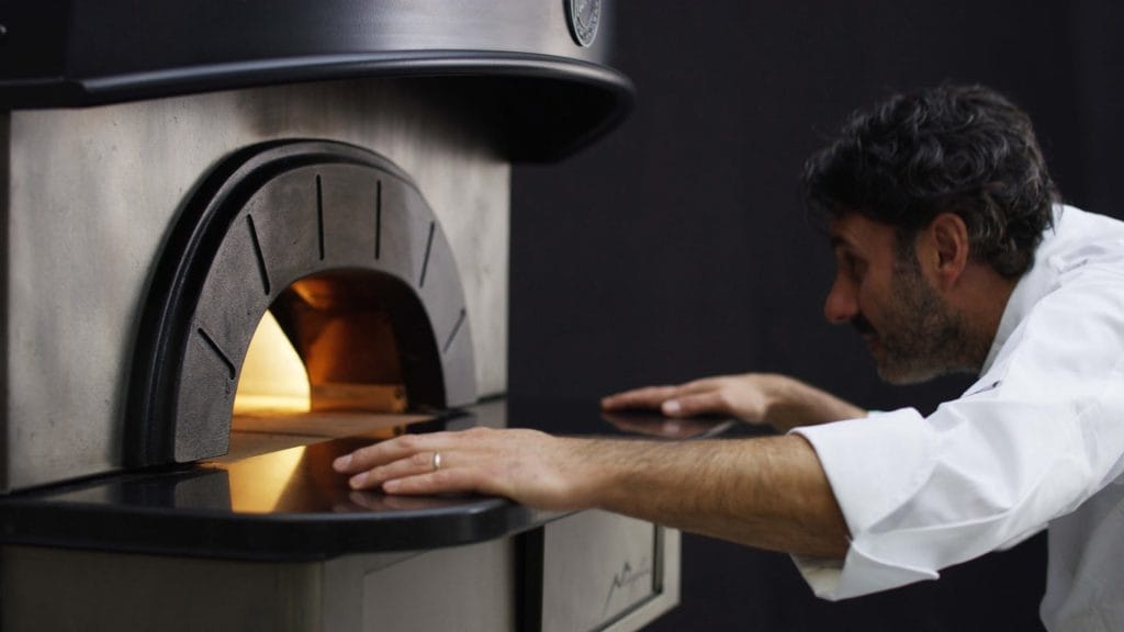 mann undersøker pizza i profesjonell pizzaovn til restaurant